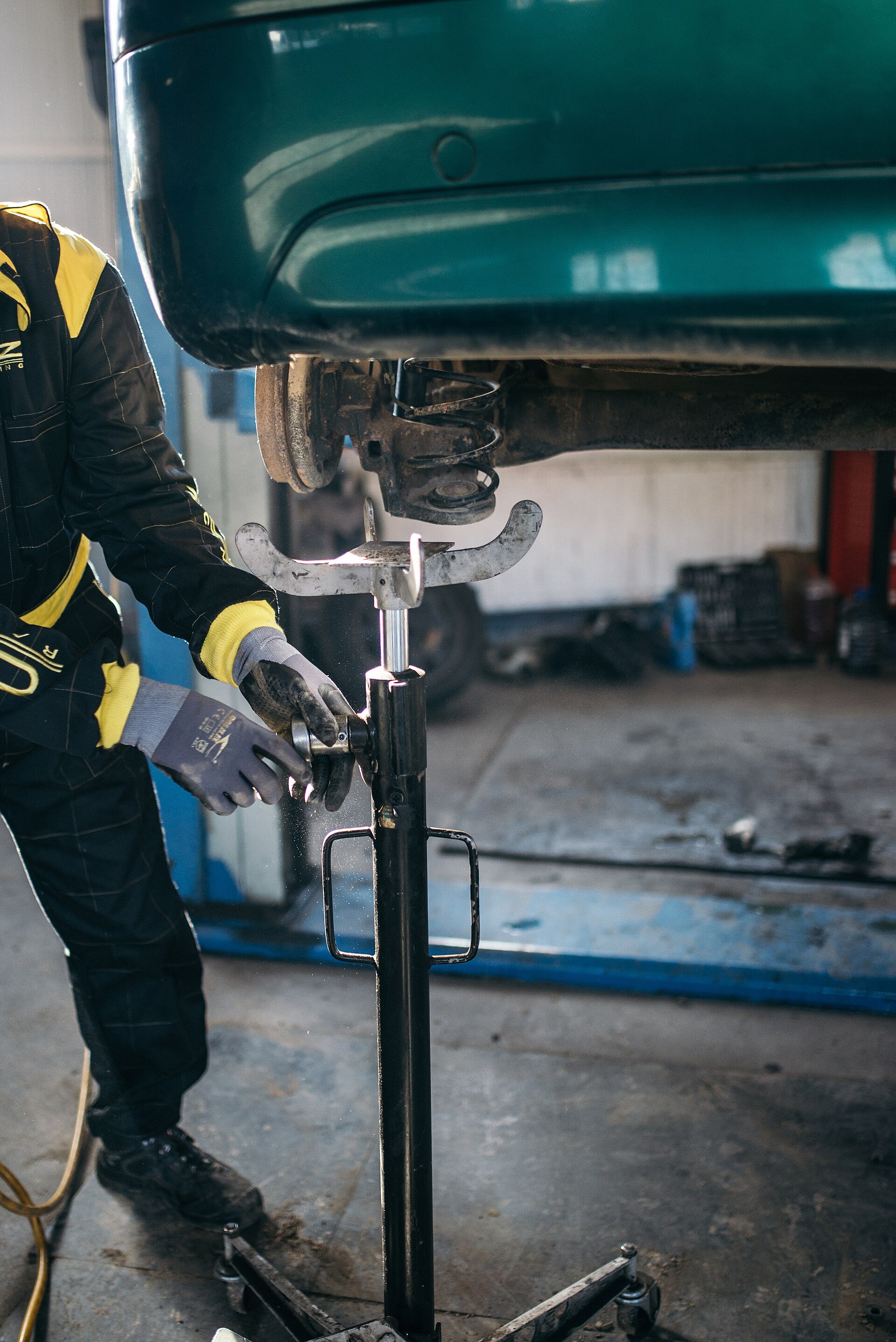 A mechanic adjusting a jack under a lifted car in a repair shop.