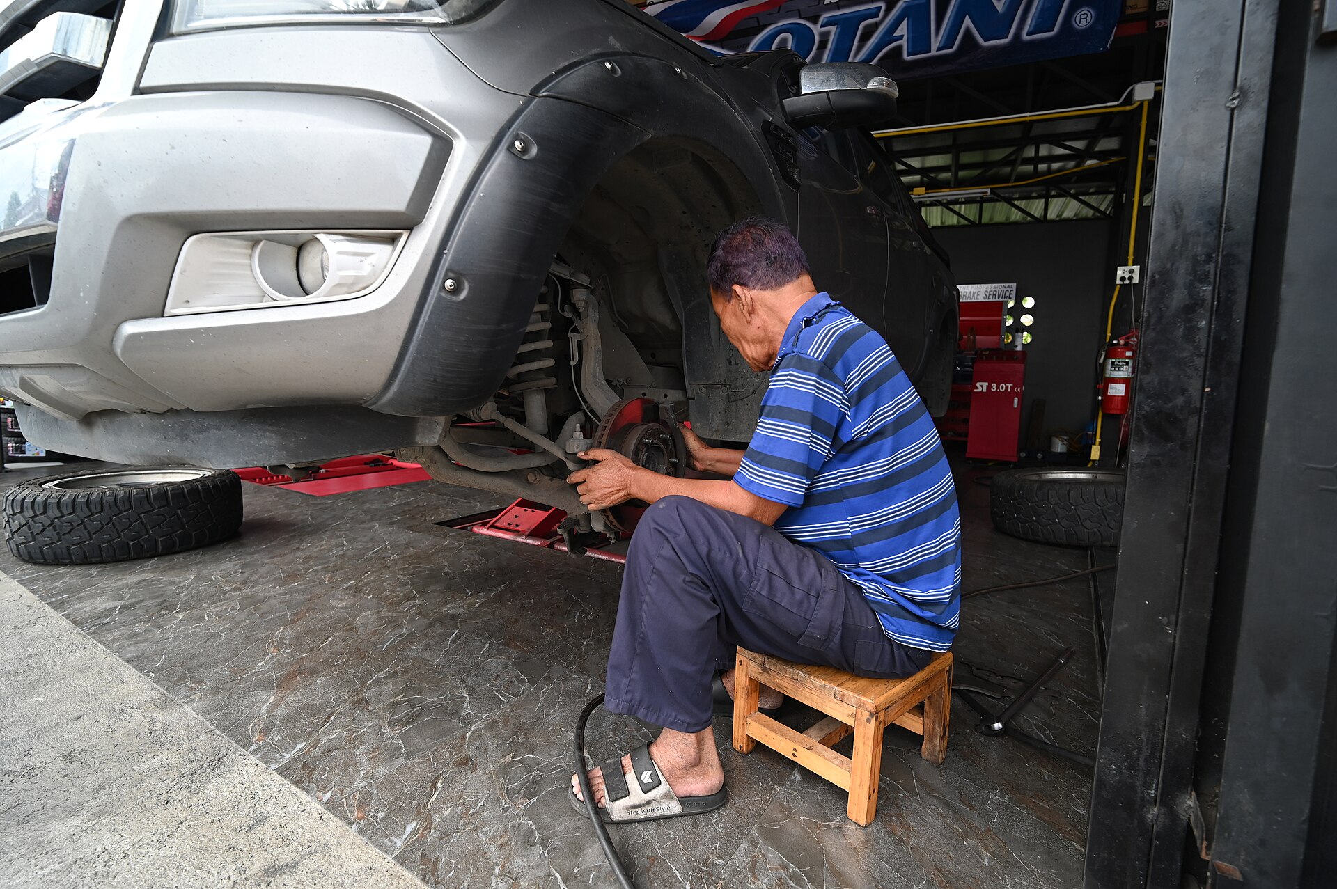 A mechanic on a wooden stool working on a pickup's front brakes.